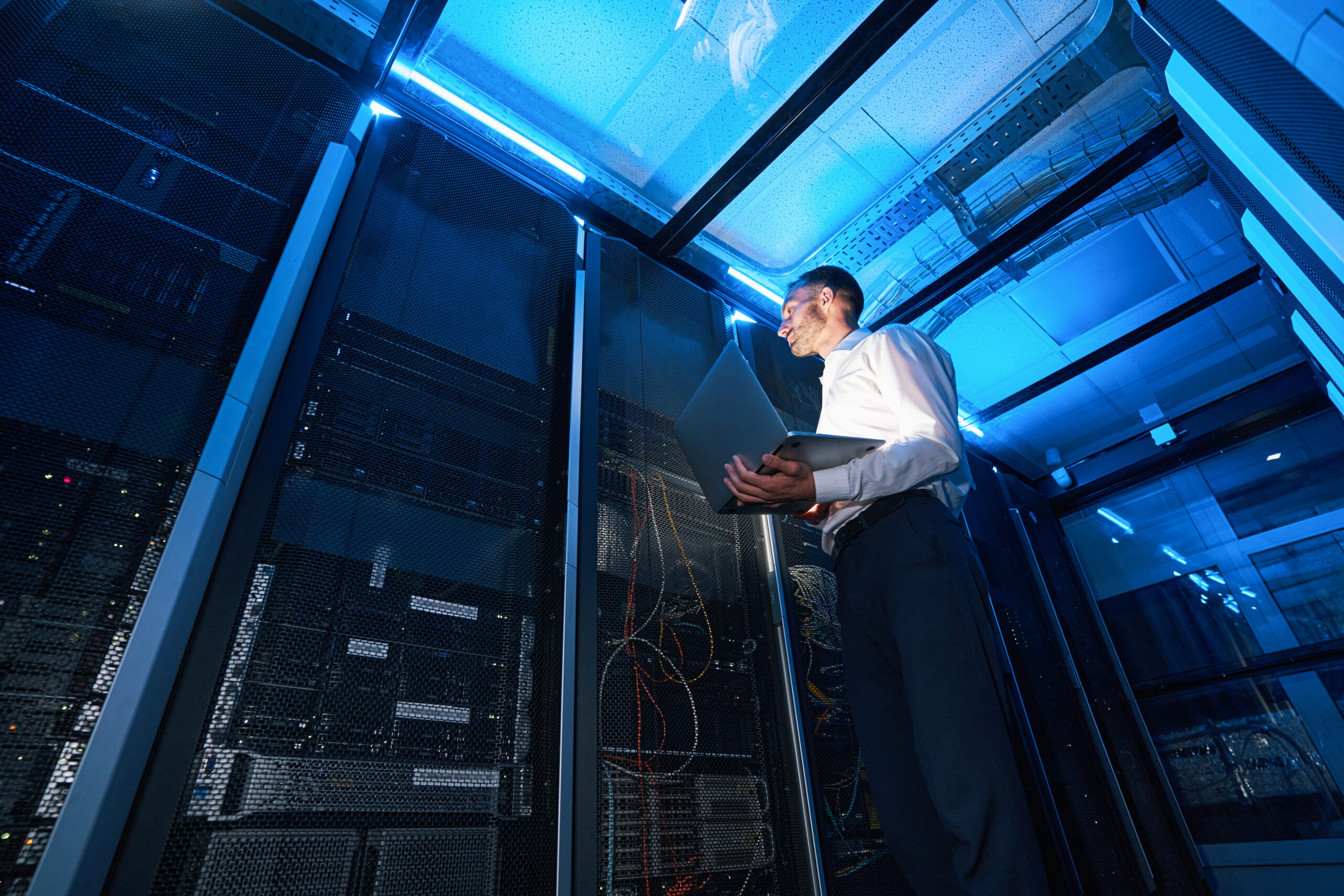 Mann steht im Server-Raum, um Computernetze und Systeme und Porzesse auf Schwachstellen hin zu überprüfen.