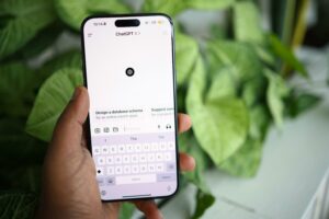 Hand hält Smartphone mit geöffneter ChatGPT-App vor grünem Pflanzenhintergrund