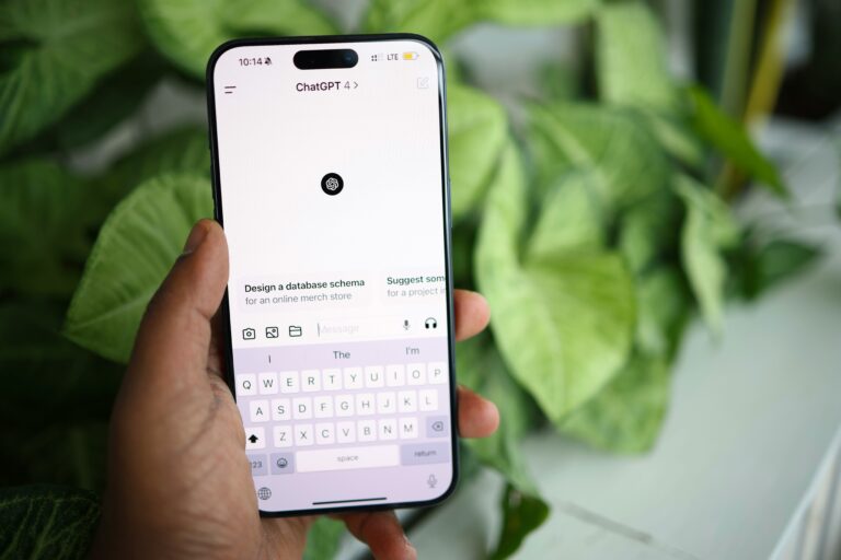 Hand hält Smartphone mit geöffneter ChatGPT-App vor grünem Pflanzenhintergrund